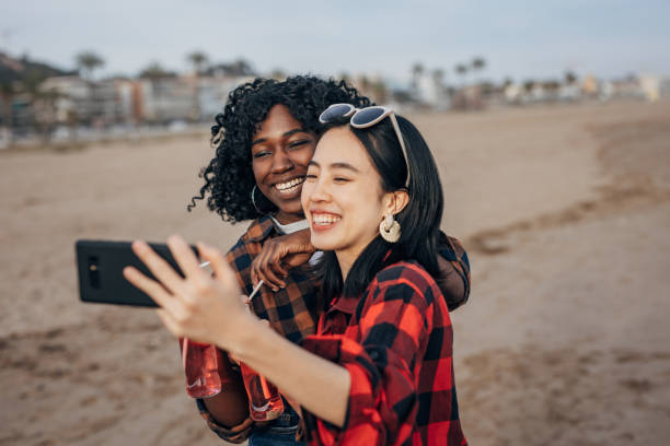 istock Two friends walking the beach drinking soda and taking a selfie 1389860182