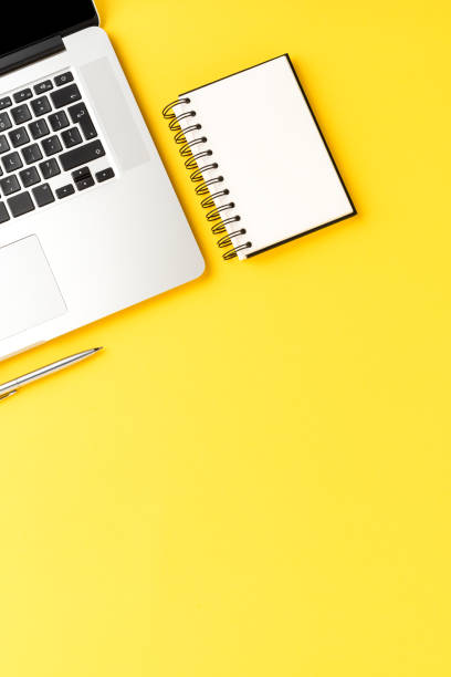 istock Elegant office desktop with laptop, notebook and pen on yellow background with copyspace. Modern workspace 1389860820