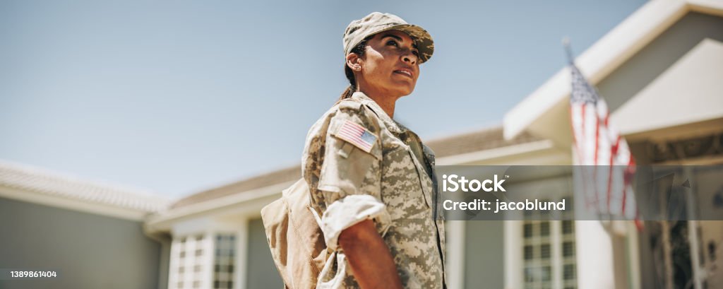 Courageous female soldier returning home from the army Courageous female soldier looking away thoughtfully while standing outside her house with her bag. American servicewoman coming back home after serving her country in the military. Military Stock Photo