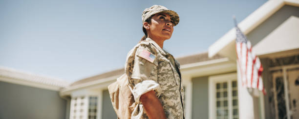 Courageous female soldier returning home from the army Courageous female soldier looking away thoughtfully while standing outside her house with her bag. American servicewoman coming back home after serving her country in the military. veteran stock pictures, royalty-free photos & images