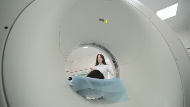 Female patient in mask is undergoing CT or MRI scan in modern medical clinic. Patient lying on a CT or MRI scan table, enters in machine
