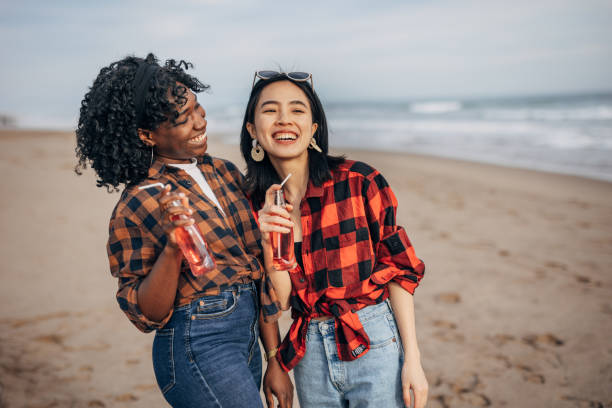 istock Two hipster friends walking on the beach and drinking soda 1389862588