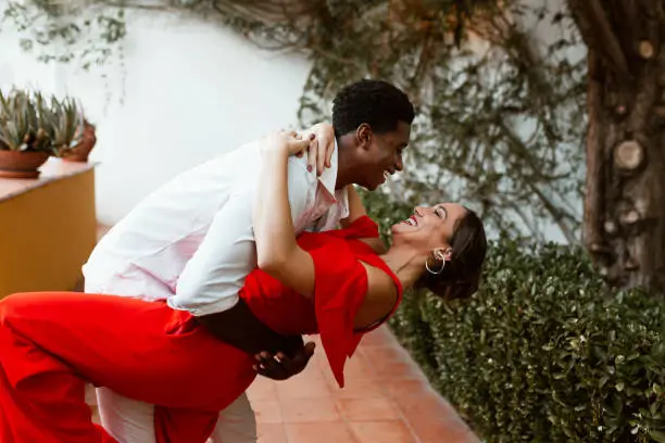 Loving couple dancing in their backyard at home. Young interracial couple laughing cheerfully during a tango. Happy young couple sharing a fun and romantic moment together.