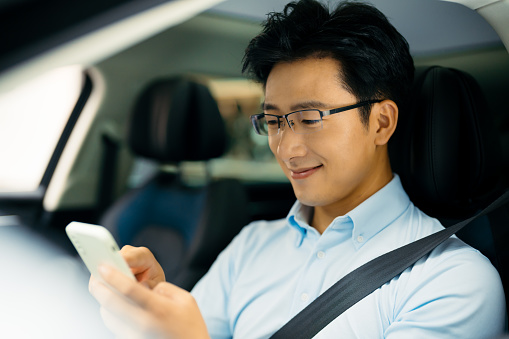 Young Asian man  using smart phone and enjoying new car.