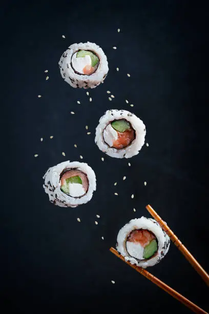 Levitation or flying of rolled sushi Japanese dish prepared with boiled rice and nori seaweed filled with mascarpone cheese, cucumber or avocado and raw tuna or salmon fish served with chopsticks