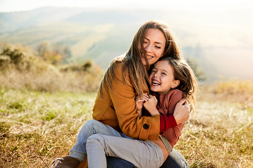 Playful mother having fun with her small girl during autumn day in a meadow.