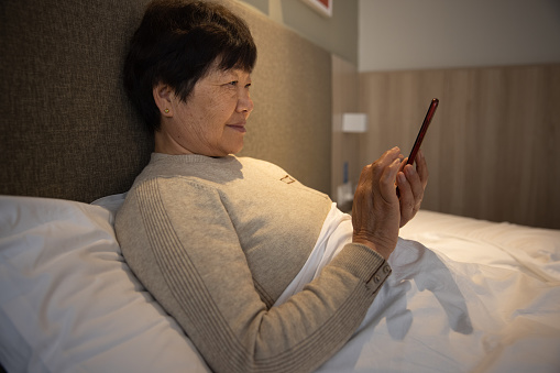 Senior woman using phone lying on bed