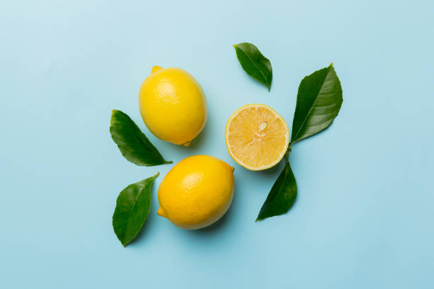 istock Many fresh ripe lemons with green leaves on colored background, top view, space for text 1389874513