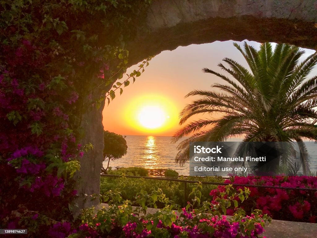 Sunset on the island of Ischia (Golfo di Napoli, Italy) The photo was taken at the island of Ischia, at the beginning of summer. It shows the sun setting down at the horizon, as seen across an arch surrounded by flowers and plants. Ischia Island Stock Photo