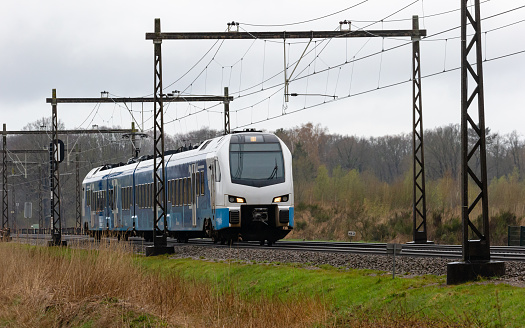 Enschede, Twente, Overijssel, Netherlands, april 5th 2022, white/blue KEOLIS stop train passing by, coming from Enschede driving in the direction of the city Hengelo -KEOLIS is a French, Paris based company operating in the public transportion industry, the Dutch KEOLIS trains were formerly owned by Connexxion, branded under the name \