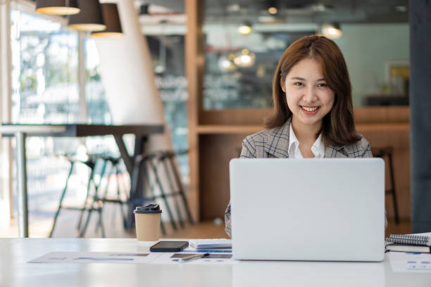 istock Beautiful Asian businesswoman analyzing chart using calculator, laptop at the office with papers and holding pen, sitting on the chair at modern home studio. Mobile worker contacting customers 1389877043