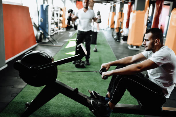 istock Athletic Male Using Rowing Machine For Workout With Friends 1389879178
