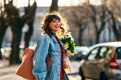 Happy woman with dental braces holding bouquet of flowers and walking at the city street.