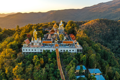 Wat Phrathat Doi Kham in Chiang Mai, Thailand. Temple atop a forested mountain featuring ornate gold carvings and a 17m sitting Buddha statue.