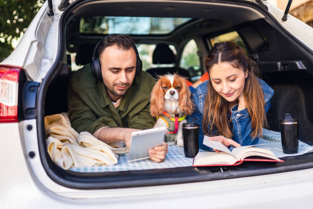 image of young couple and their dog camping in the trunk of their car reading a book and drinking coffee - white dog audio imagens e fotografias de stock