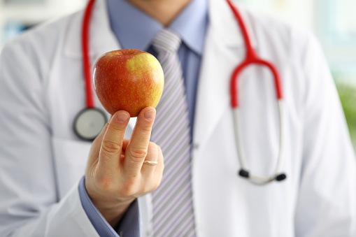 Male medicine therapeutist doctor hands holding red fresh ripe apple. Medical help or insurance concept. Health life and wholesome food concept. Vegetarian lifestyle concept. Fruits and vitamins