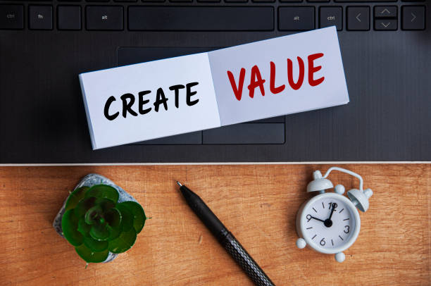 istock Create value text on notepad with laptop, clock, pen and wooden background. Business concept 1389885823