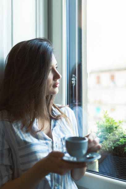 istock Woman by the window drinking a coffee in the cup 1389885980