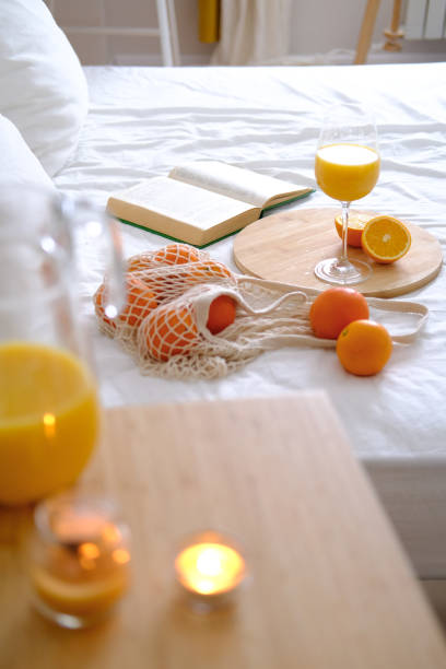 Oranges and orange juice in a glass on a white bed. Fresh oranges. Fruits lie on a white bed. Fruits close-up. Breakfast in bed.