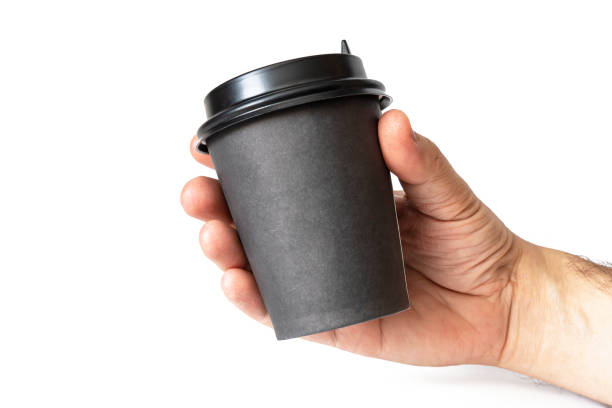 istock Black paper coffee mug in a man's hand on a isolated white background. Empty space for text and design. The form for the name of the coffee or company or coffee shop 1389888514