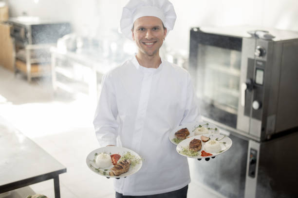 istock Smiling chef in uniform standing with ready meals in the kitchen 1389888739