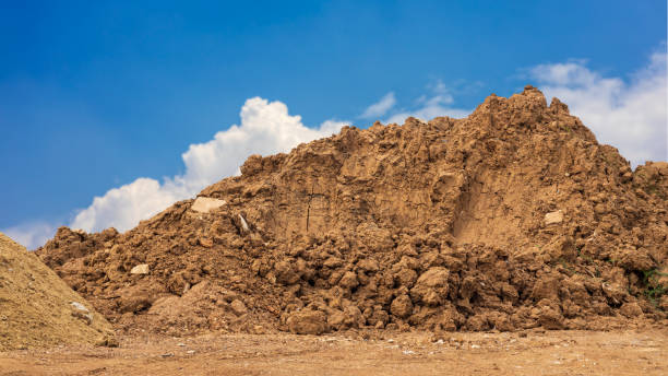 View of brown mounds dug up and dumped on the ground waiting to prepare for the landfill. View of brown mounds dug up and dumped on the ground waiting to prepare for the landfill to improve construction with clouds in the sky in the background. gravel mound stock pictures, royalty-free photos & images