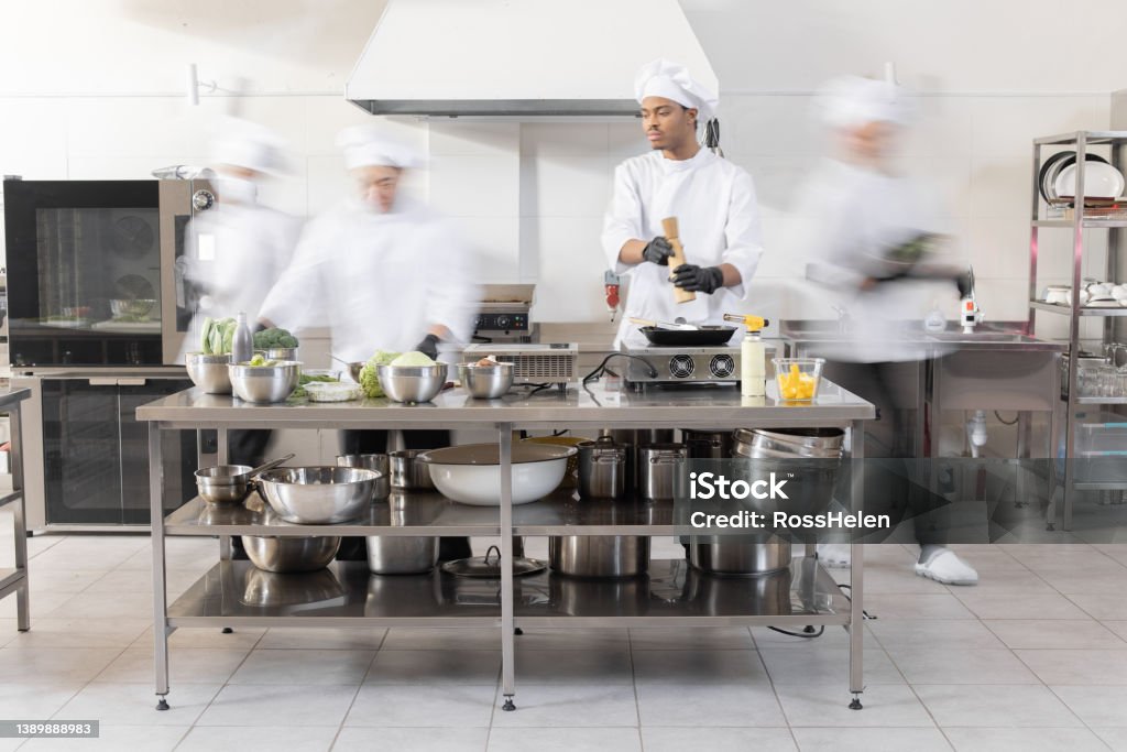 Chef cooks working in professional kitchen Chef cooks working in professional kitchen. Chefs hurry up, actively cooking meals for restaurant. Long exposure with motion blurred figures Commercial Kitchen Stock Photo