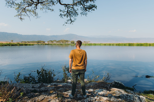 One man explorer enjoying safari trip staying at the lakeshore with a view of hippo floating in the water with mountain view