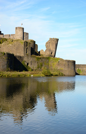 Caerphilly, Wales - August 2017: Walls and leaning tower of the medieval castle, with the waters of the moat in the foreground