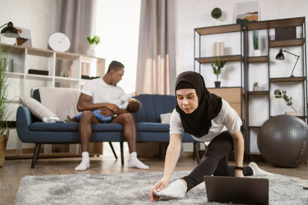 頭に頭にスカーフを巻いたアラブ人女性が自宅のリビングルームで体操をしている - yoga business women living room ストックフォトと画像