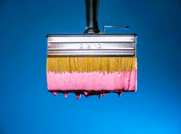 Wet dripping pink paintbrush closeup on blue background
