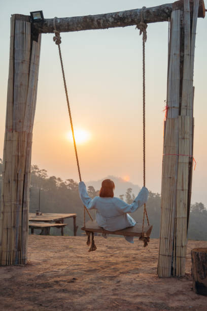 Loneliness woman sitting on the swing and looking at the sun at sunrise time. stock photo