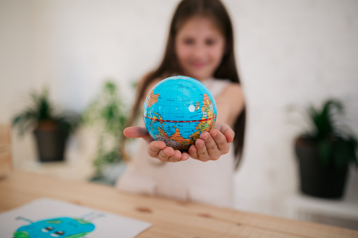 Happy Caucasian little girl celebrating earth day at home, holding a toy globe in her hands and smiling