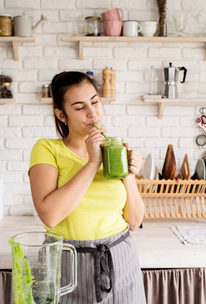 istock Young brunette woman drinking green smoothie at home kitchen 1389897953