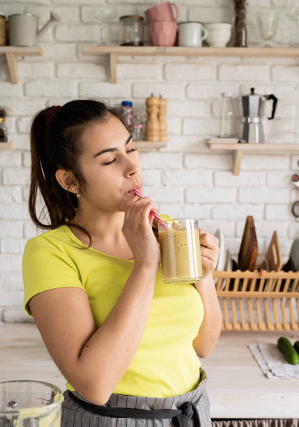 istock Young brunette woman drinking fruit banana smoothie at home kitchen 1389898192