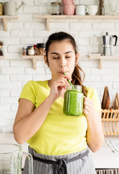 istock Young brunette woman drinking green smoothie at home kitchen 1389898362