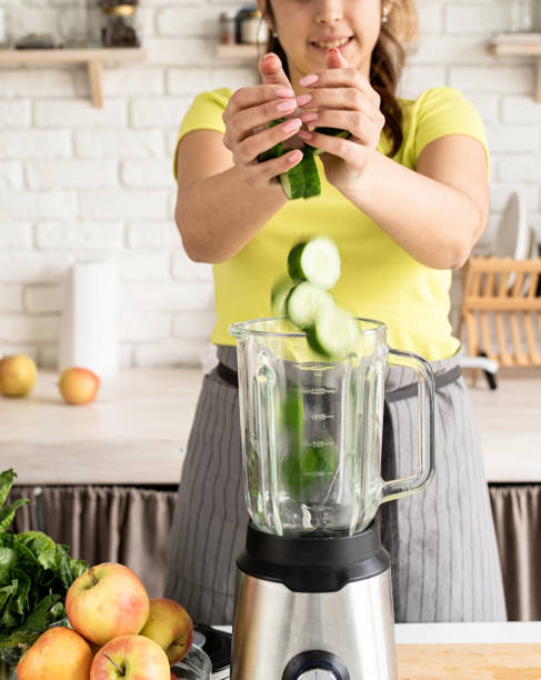 istock Young woman making green cucumber smoothie at home kitchen 1389898625
