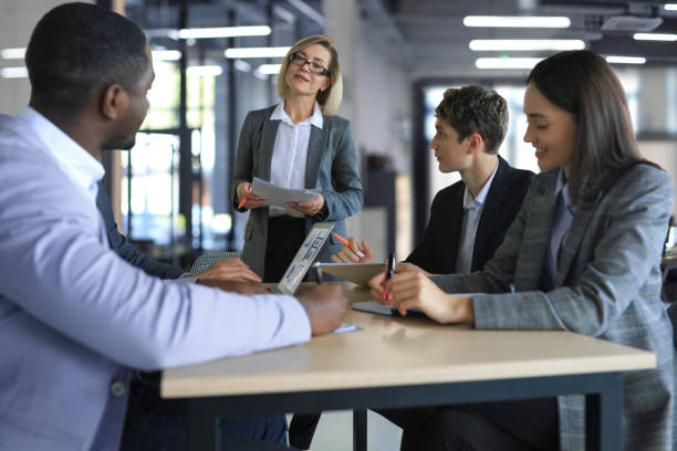 istock Female boss addressing meeting around boardroom table. 1389900040