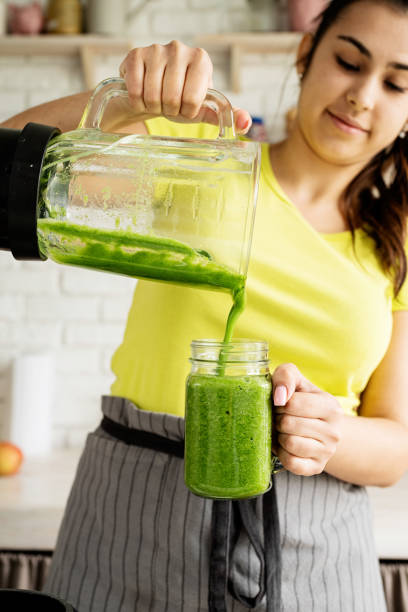 istock Young brunette woman making green smoothie at home kitchen 1389900077