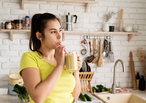 istock Young brunette woman drinking fruit banana smoothie at home kitchen 1389901379