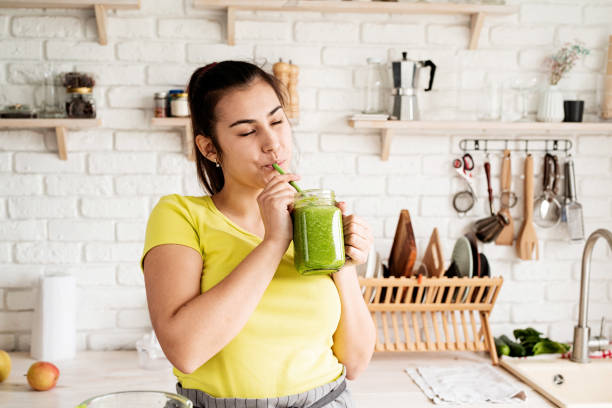 istock Young brunette woman drinking green smoothie at home kitchen 1389902105