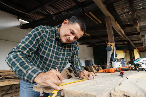 Hispanic carpenter working in his workshop - man working with carpentry tools - happy carpenter working
