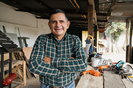 Hispanic carpenter smiling proud in wood shop of him - Proud owner of carpentry shop standing with arms crossed