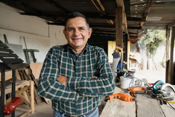 Photo of Hispanic carpenter smiling proud in wood shop of him - Proud owner of carpentry shop standing with arms crossed