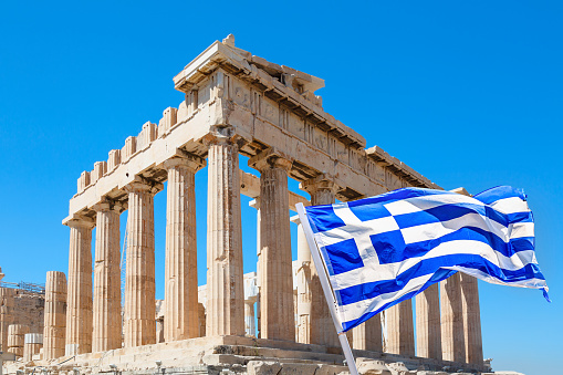 World famous iconic Parthenon on the Acropolis Hill in Athens, Greece with Greek flag against blue sky.