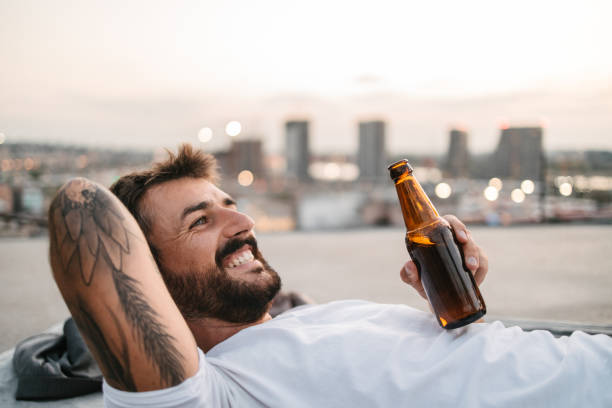 屋上で笑いながらビールを飲む青年 - after work beautiful people beer beer bottle ストックフォトと画像