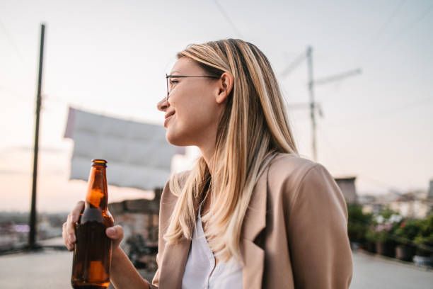 jeune femme d’affaires buvant de la bière sur un toit après le travail - after work beautiful people beer beer bottle photos et images de collection