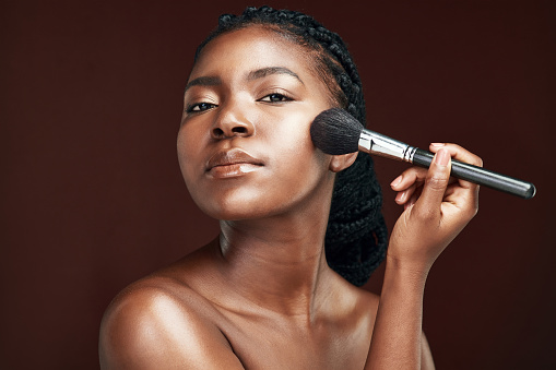 Studio shot of an attractive young woman applying makeup against a brown background