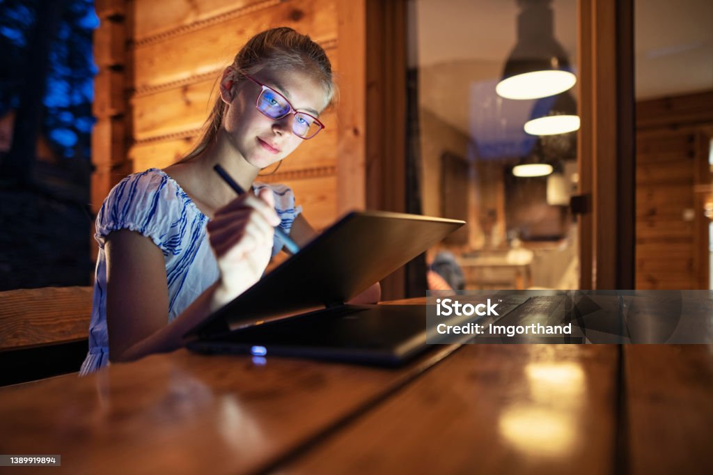 Teenage girl enjoying drawing on modern laptop Teenage girl sitting outdoors on patio and using digital pen to draw on modern laptop.
Night time.
Nikon D850 Drawing - Activity Stock Photo