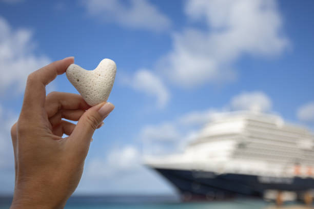 weibliche hand mit kleinem herz aus korallen auf dem hintergrund des kreuzfahrtschiffes. - kreuzfahrt stock-fotos und bilder